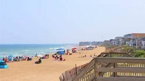 Una playa con gente, sombrillas y un paseo marítimo de madera.
