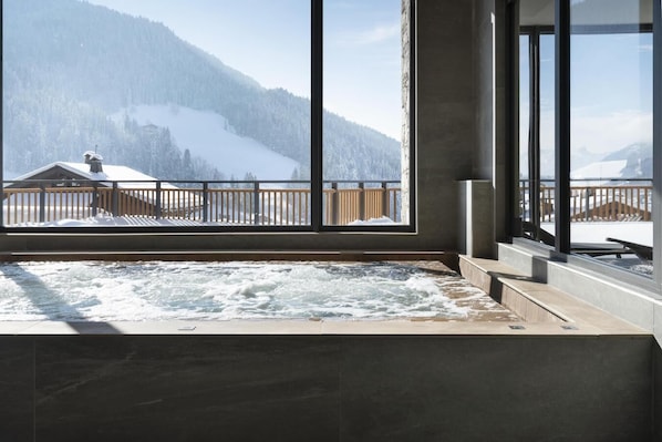 A spa area with a hot tub, large windows, and a view of snow-covered mountains.
