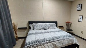 Un dormitorio con cama, una silla y una estantería en la pared.