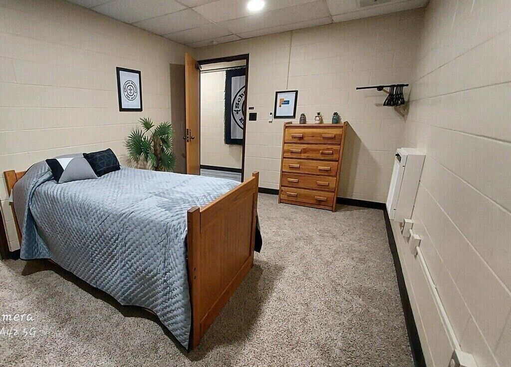 A bedroom with a bed, a dresser, a door, and a wall-mounted shelf.