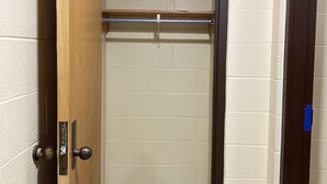 Un pasillo estrecho con una puerta de madera a la izquierda, una barandilla de metal y una pared color beige.