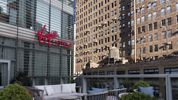 A hotel with a modern glass facade, a rooftop seating area with outdoor furniture, and a sign reading "Virgin Hotels".
