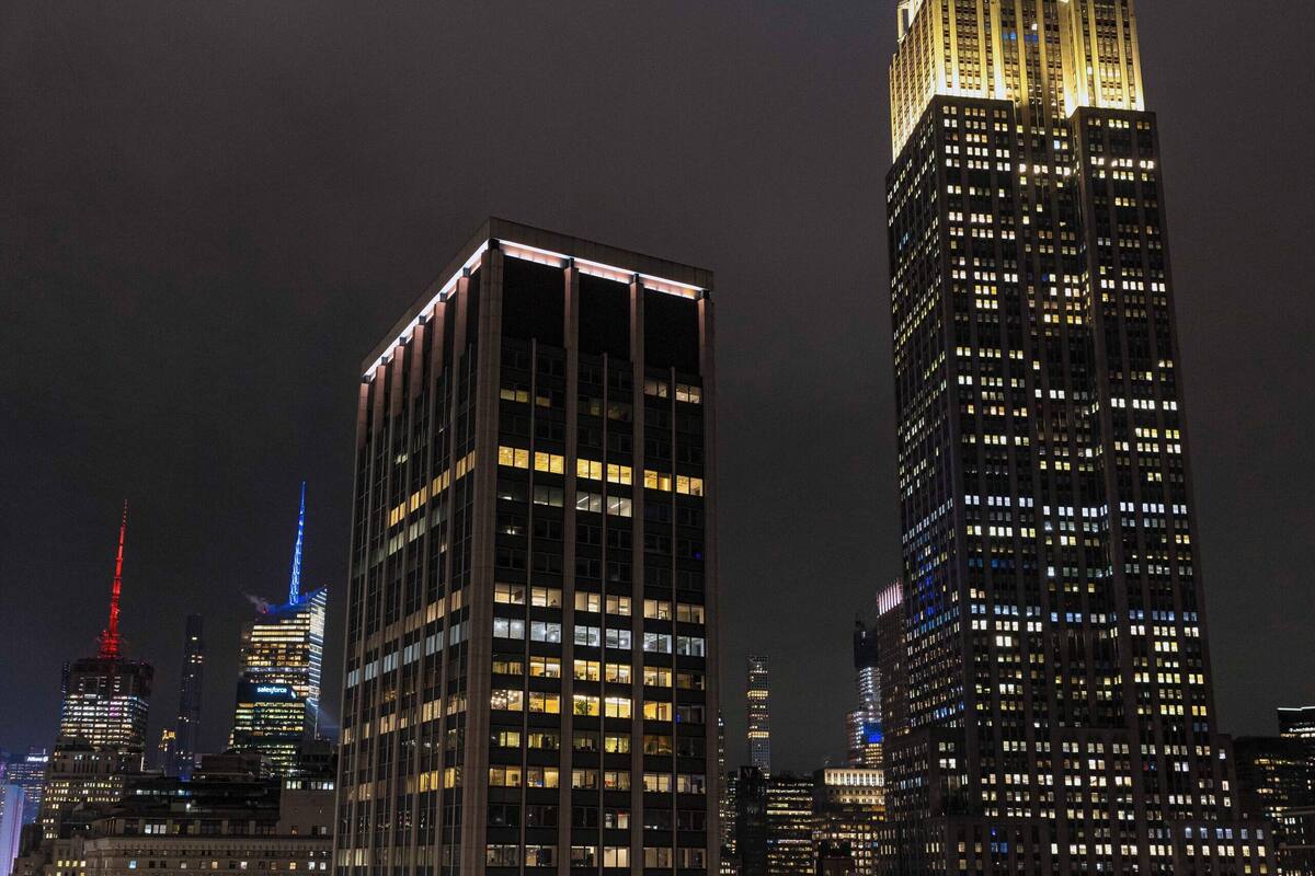 Eine Dachterrasse mit moderner Möblierung, Blick auf das Empire State Building und weitere beleuchtete Wolkenkratzer.