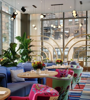 A modern hotel room with a large bed, a smaller bed, a round table, and a city view through large windows. at Virgin Hotels New York City