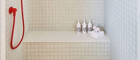 Pequeno espaço de duche revestido a azulejos, com um chuveiro de cor vermelha e um banco.