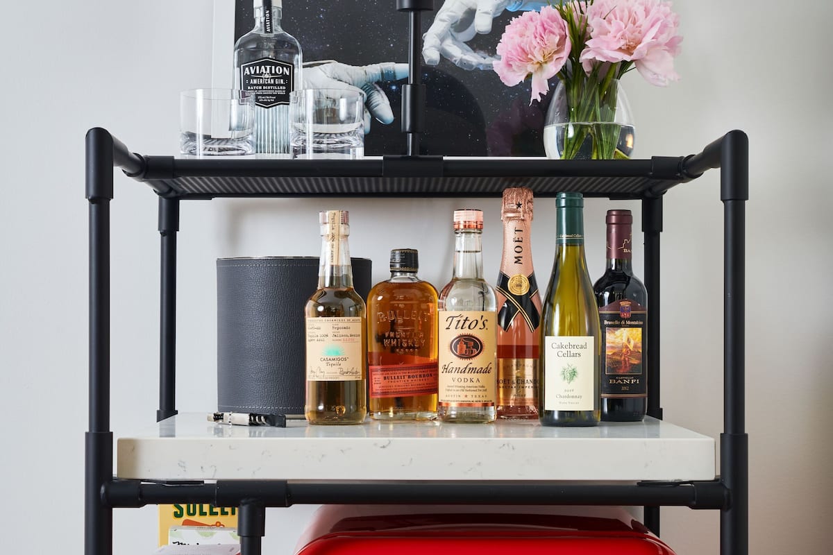 Ein roter Smeg-Kühlschrank mit einem darüberliegenden Regal, auf dem verschiedene alkoholische Getränke und ein gerahmtes Bild stehen.