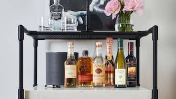 A red Smeg refrigerator with a shelf above it holding various bottles of alcohol and a framed picture.