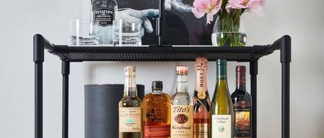 A red Smeg refrigerator with a shelf above it holding various bottles of alcohol and a framed picture.