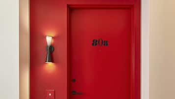 A red door with a number plate, a wall-mounted light fixture, and a power outlet.