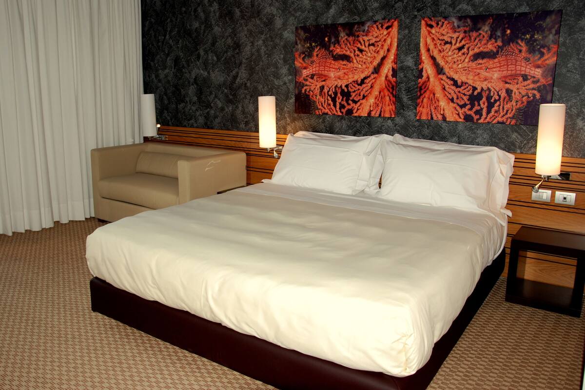 Une chambre d’hôtel avec un grand lit, un canapé, deux lampes fixées au mur et des œuvres d’art sur le thème des coraux.