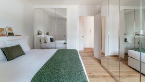 Een moderne slaapkamer met een groot bed, een groene plaid, een geel hanglamp en een garderobe met spiegel.