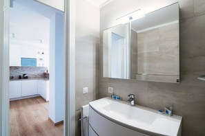 A modern bathroom with a large mirror, a white sink, and a shower area. - Palace Apartment (Lugano)