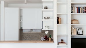 Een moderne keuken met witte kasten, een granieten aanrechtblad en een inbouwboekenkast met boeken en decoratieve objecten.
