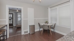 A modern kitchen with a dining area, featuring a built-in oven, a small trash bin, and a ceiling light fixture.