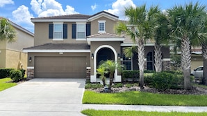 A two-story house with a brown garage, a front porch, and a well-maintained lawn with palm trees.