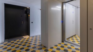 En gang med en sort dør, en lysegrå væg og en elevator med spejllignende overflade.