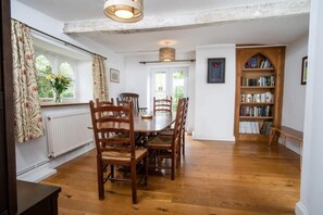 Un coin repas avec une table et des chaises en bois, une bibliothèque et une fenêtre avec des rideaux.