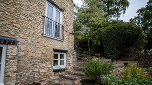 A stone building with a small window and steps leading to a garden area. - Beautiful Cotswolds Cottage & Garden (Horsley)