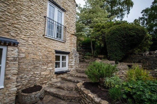 A stone building with a small window and steps leading to a garden area. - Beautiful Cotswolds Cottage & Garden (Horsley)