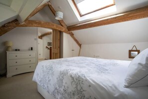 Ein Schlafzimmer mit schrägemausertem Dach, einem Bett mit Blumenmuster auf der Bettdecke, einem Schminktisch und einem Dachfenster.