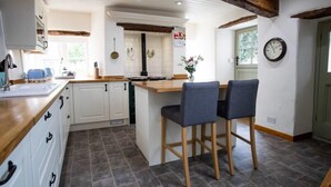 A kitchen with a wooden island, white cabinets, and a clock on the wall. - Beautiful Cotswolds Cottage & Garden (Horsley)