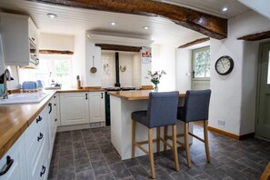Une cuisine avec un îlot central en bois, des armoires blanches et une horloge au mur.