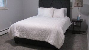 Een slaapkamer met een bed, nachtkastje, lamp en raam.