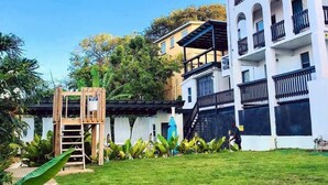 Um edifício com vários andares, varandas e uma pequena estrutura de recreação ao primeiro plano.