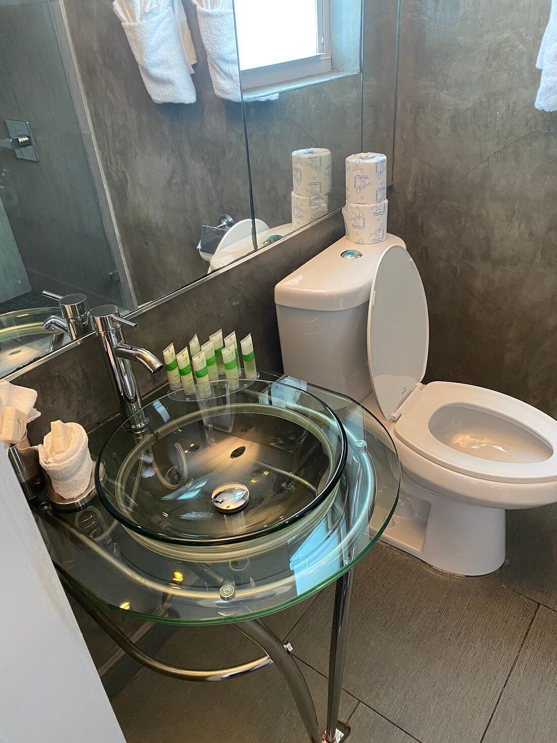 Un baño moderno con un lavabo de vidrio, un inodoro y un espejo.