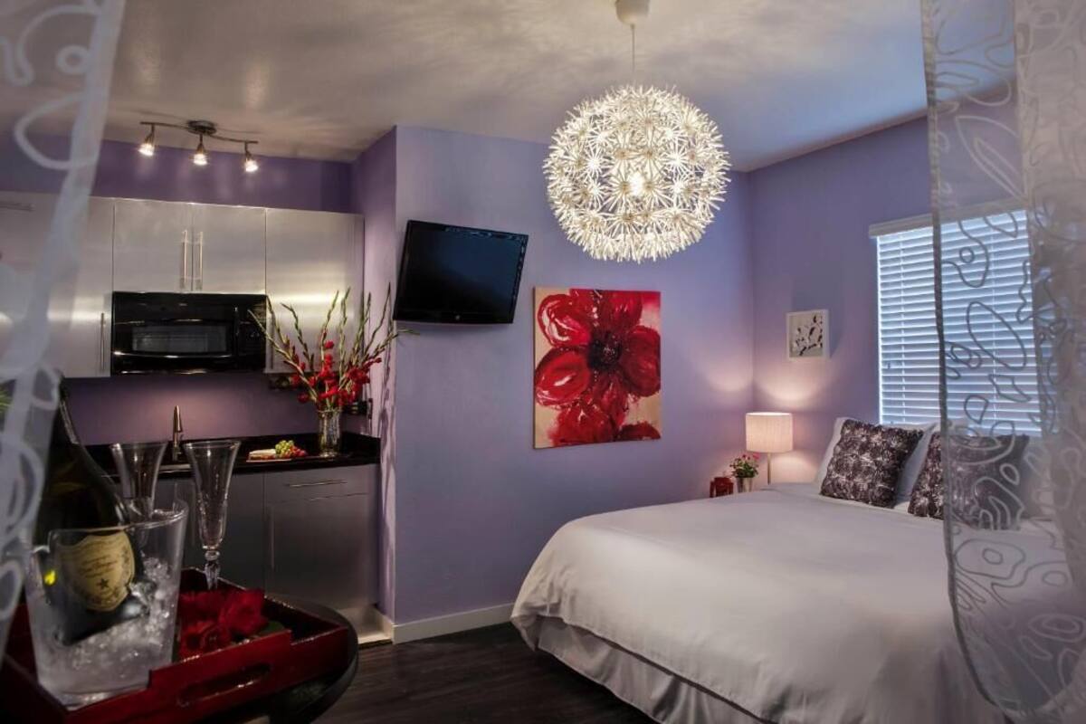 A modern bedroom with a large bed, a flat-screen TV, a decorative ceiling light, and a red floral artwork on the wall.