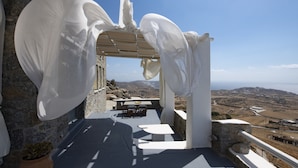 A terrace with a stone wall, a table, and a view of the landscape. - Mykonos Teatro Suites and Villa (Mykonos)