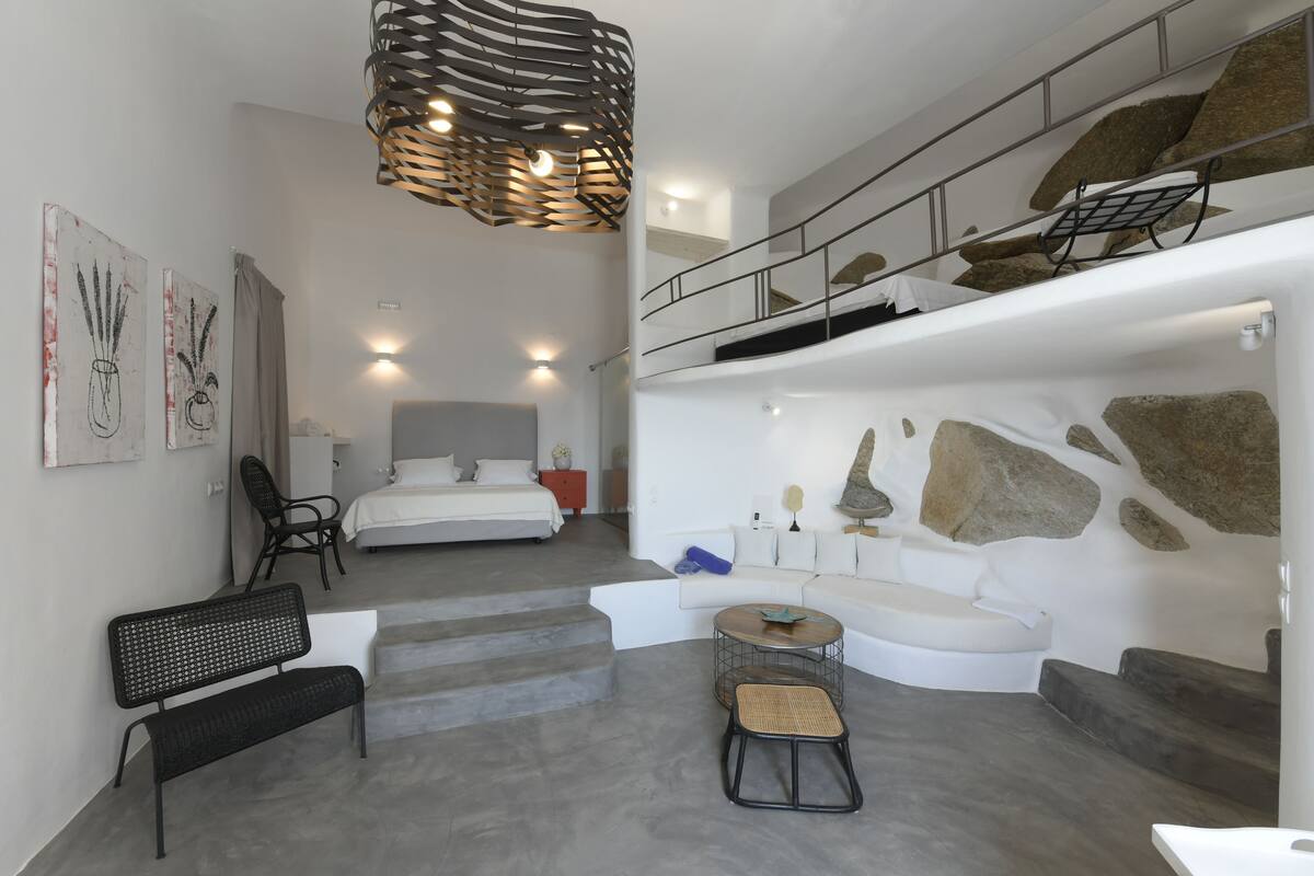 Een modern interieur met een trap naar een tweede verdieping, een witte bank, een ronde tafel en een bankje.