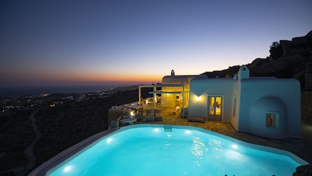 A swimming pool with a view of a coastal landscape and a building with a lighted entrance. - Mykonos Teatro Suites and Villa (Mykonos)
