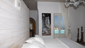 A bedroom with a large bed, a painting on the wall, and a view of the sea through a door. - Mykonos Teatro Suites and Villa (Mykonos)