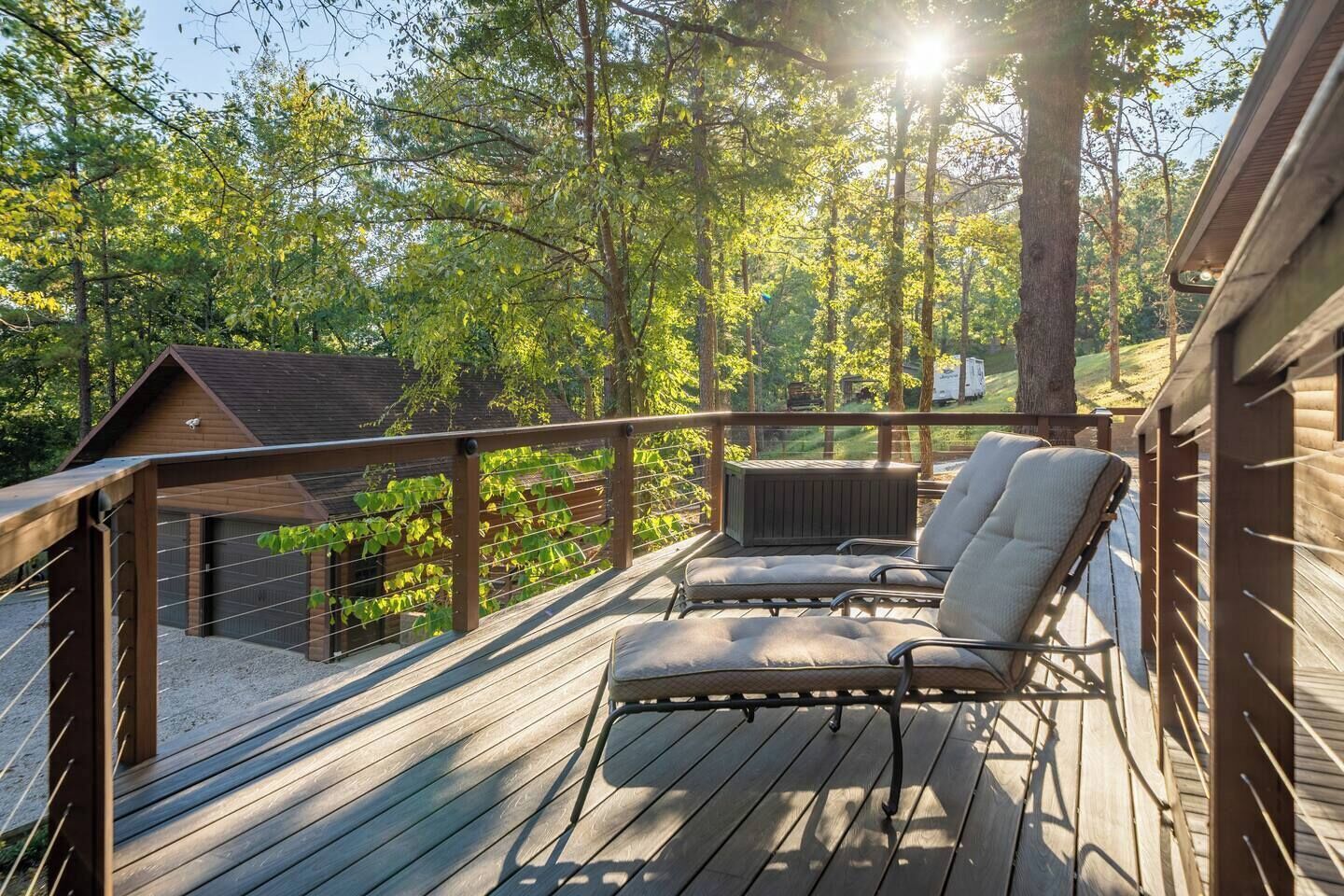 A wooden deck with two cushioned chairs and a small heater, surrounded by trees and a wooden cabin.