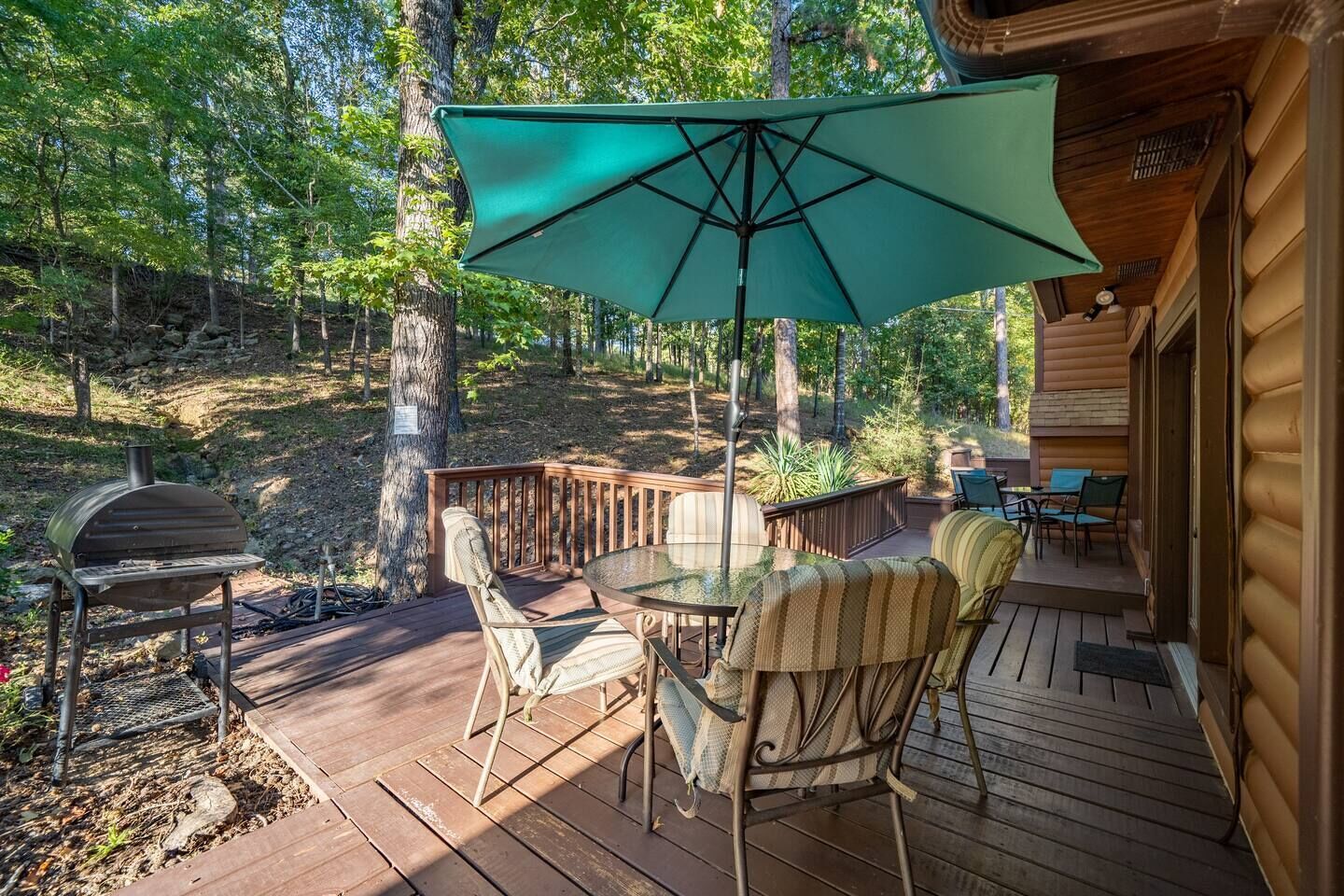 Una terraza de madera con una mesa, sillas, una parrilla y un paraguas grande.