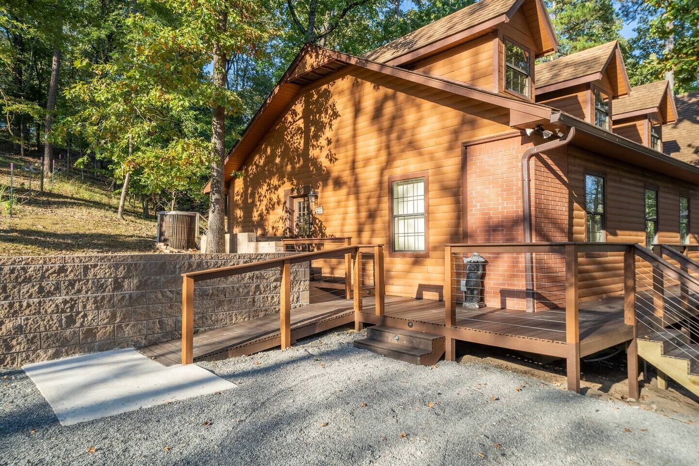 Una cabaña rústica de troncos con un muro de contención de piedra, terraza de madera y escalera que conduce a un segundo nivel.