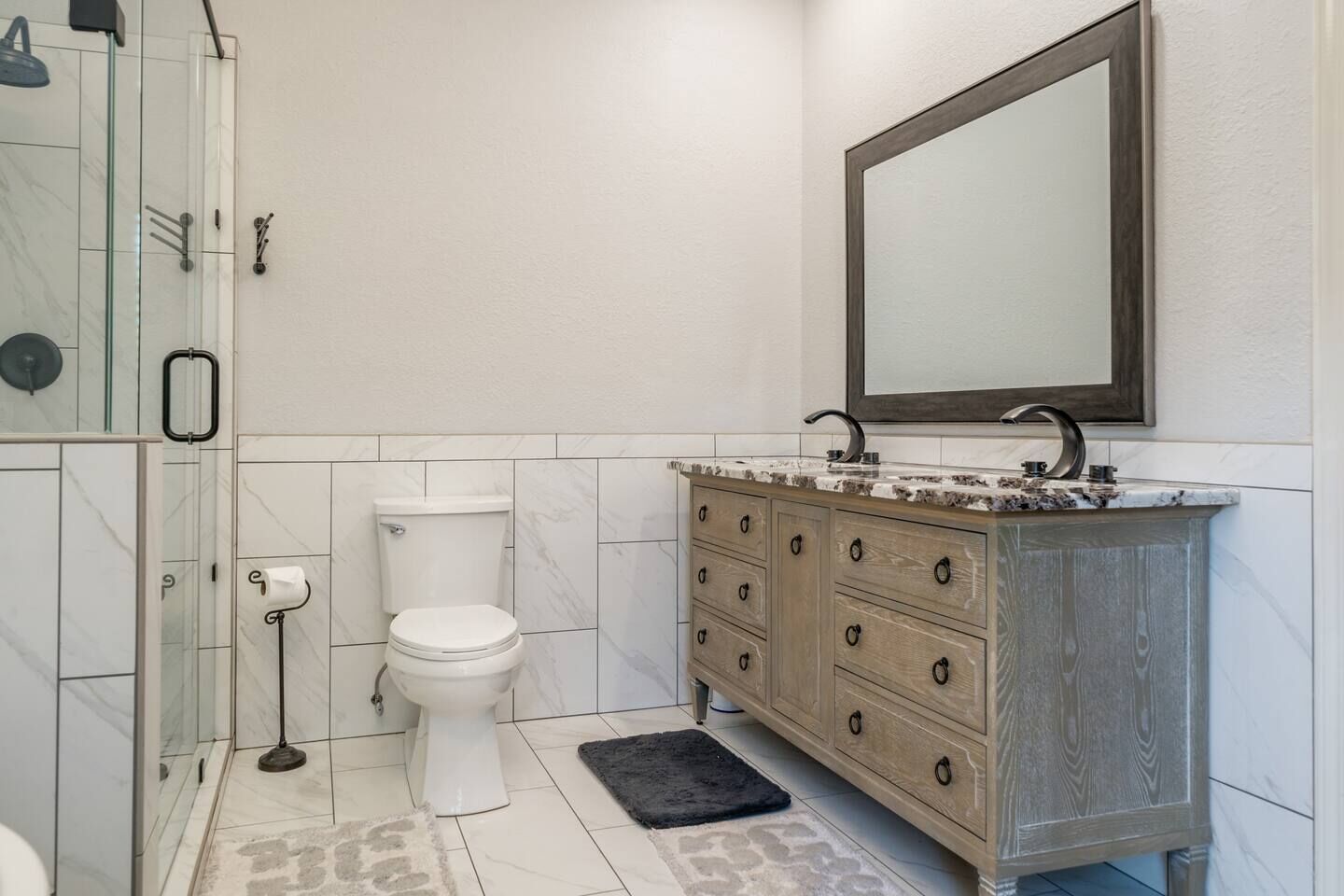 A bathroom with a toilet, vanity with drawers, a mirror, and a shower area.