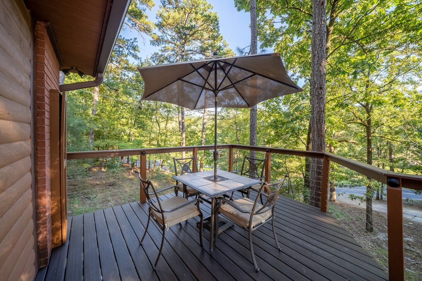 A wooden deck with a table and chairs, an umbrella, and a view of a forested area.