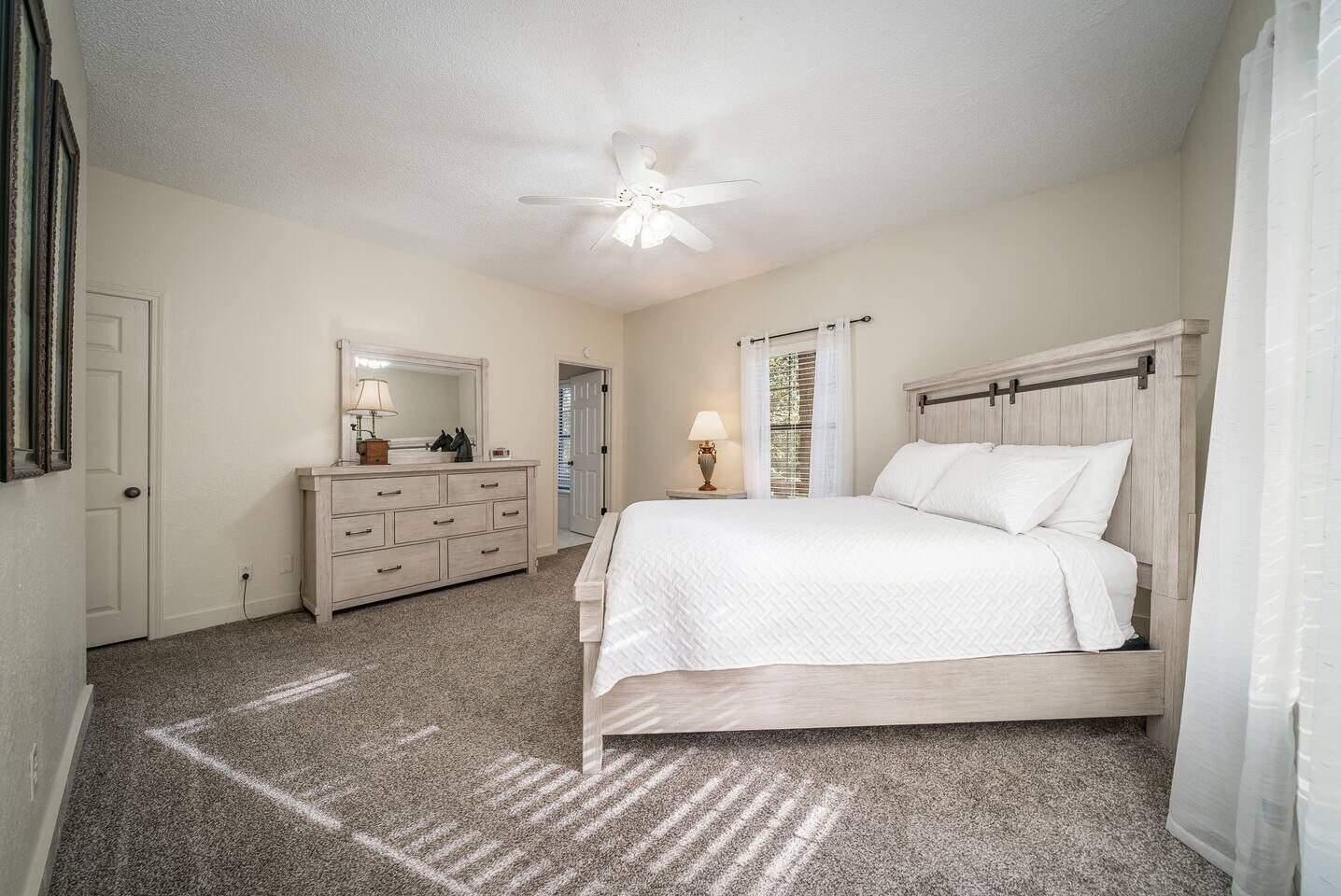 A bedroom with a bed, dresser, mirror, ceiling fan, and a door.