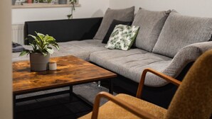 Uma sala de estar moderna com um sofá cinzento, uma mesa de centro de madeira, uma planta em vaso e um lustre.