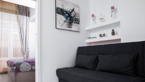 A modern living room with a dark grey sofa, a white wall with a framed abstract painting, and a white shelf with decorative items. - L&L Apartments (Split)