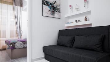Un saló modern amb un sofà grisós fosc, una paret blanca amb un quadre abstracte emmarcat, i una estanteria blanca amb objectes decoratius.