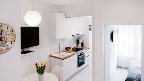 A modern kitchen with white cabinets, a wooden countertop, a sink, and a built-in oven. There is a dining table with chairs and a vase of flowers. - L&L Apartments (Split)