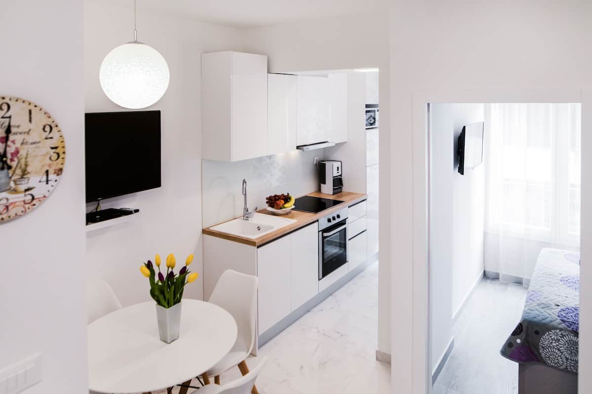 A modern kitchen with white cabinets, a wooden countertop, a sink, and a built-in oven. There is a dining table with chairs and a vase of flowers.