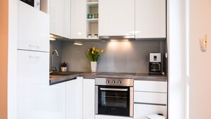A modern kitchen with white cabinets, a stainless steel oven, a coffee maker, and a vase with flowers on the countertop. - L&L Apartments (Split)
