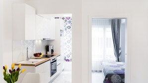 A modern kitchen with white cabinets, a wooden countertop, and a sink. There is a dining area with a white table and a vase of tulips. The room has a large window with curtains. - L&L Apartments (Split)