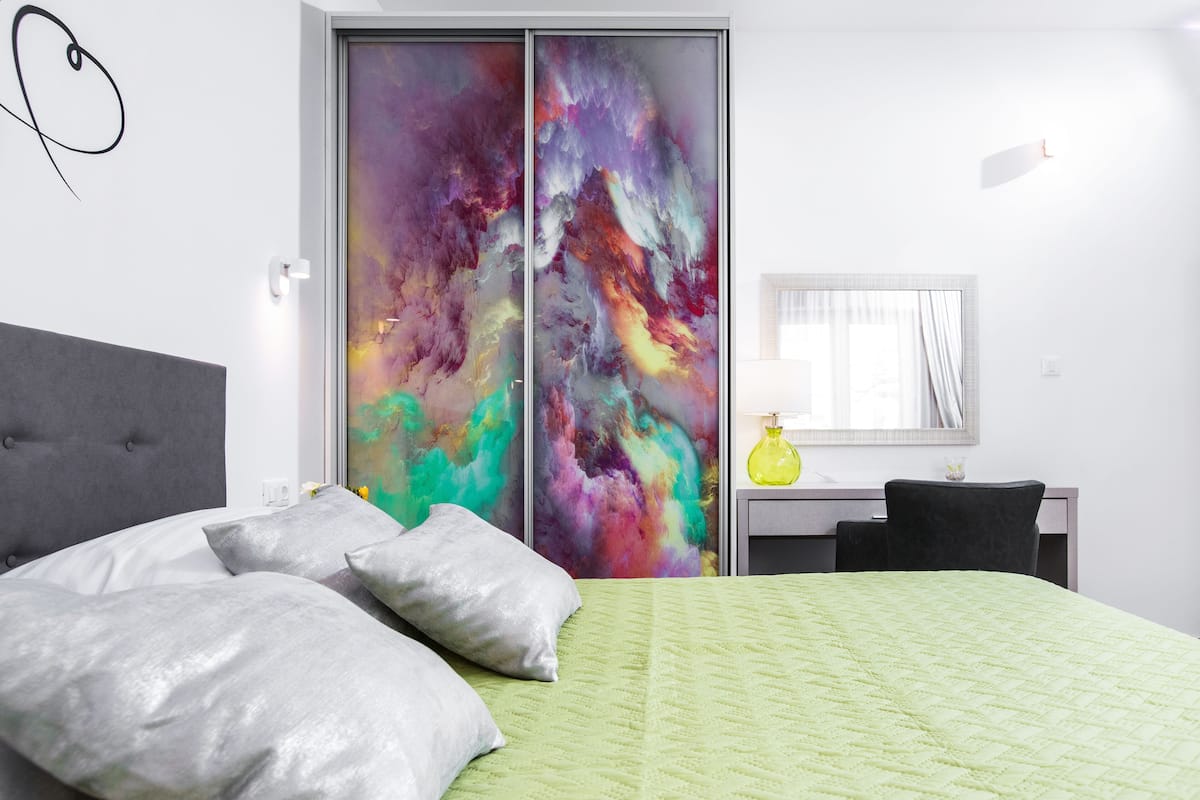 A modern bedroom with a bed, grey headboard, and a colorful abstract painting on the wall.