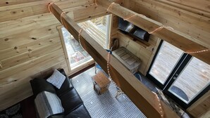 En stuga med träpanel på insidan, ett sovloft, en svart soffa och ett litet bord.