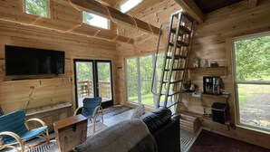 En stuga med träinredning, utrustad med en TV, sittplatser, en stege och stora fönster.